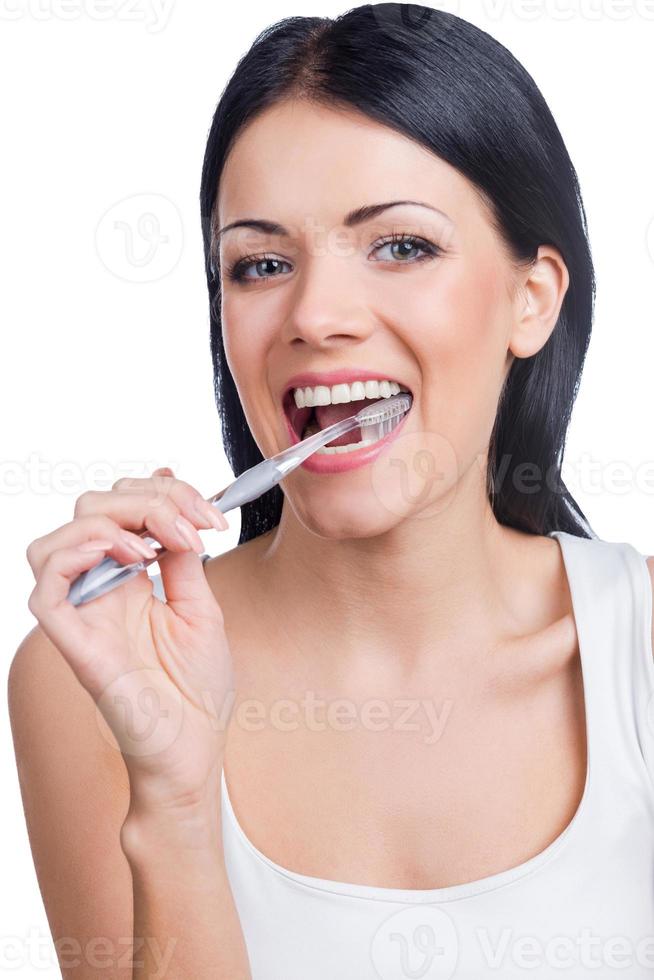 denti cura. ritratto di bellissimo giovane donna Tenere un' spazzolino nel sua bocca e guardare a telecamera mentre in piedi contro bianca sfondo foto