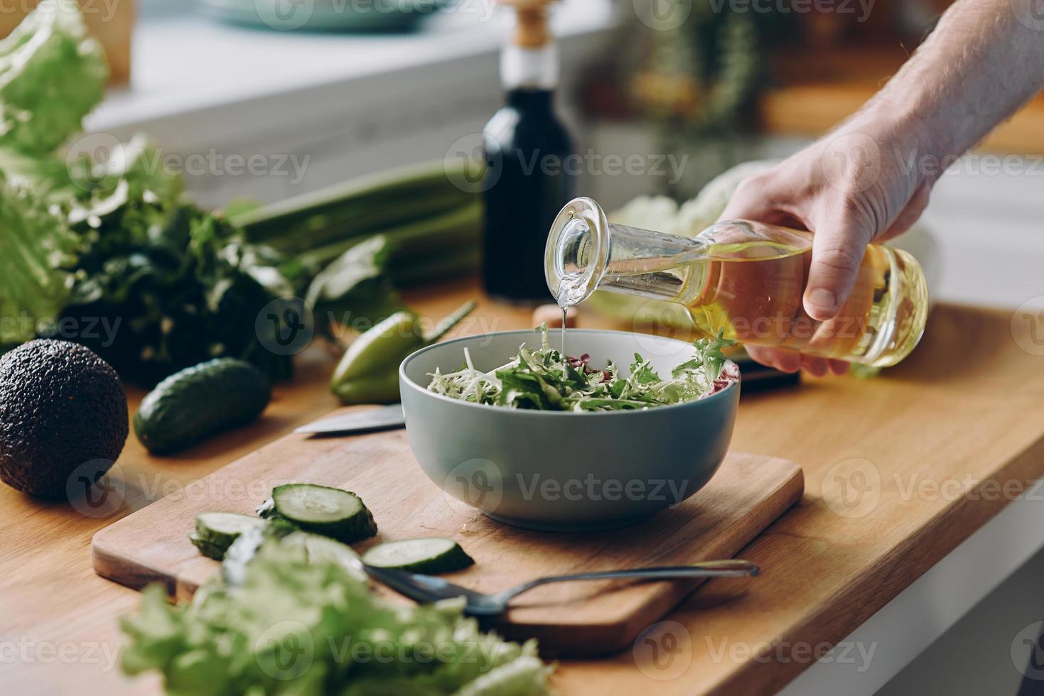 avvicinamento di irriconoscibile uomo scrosciante oliva olio in il ciotola con fresco insalata foto