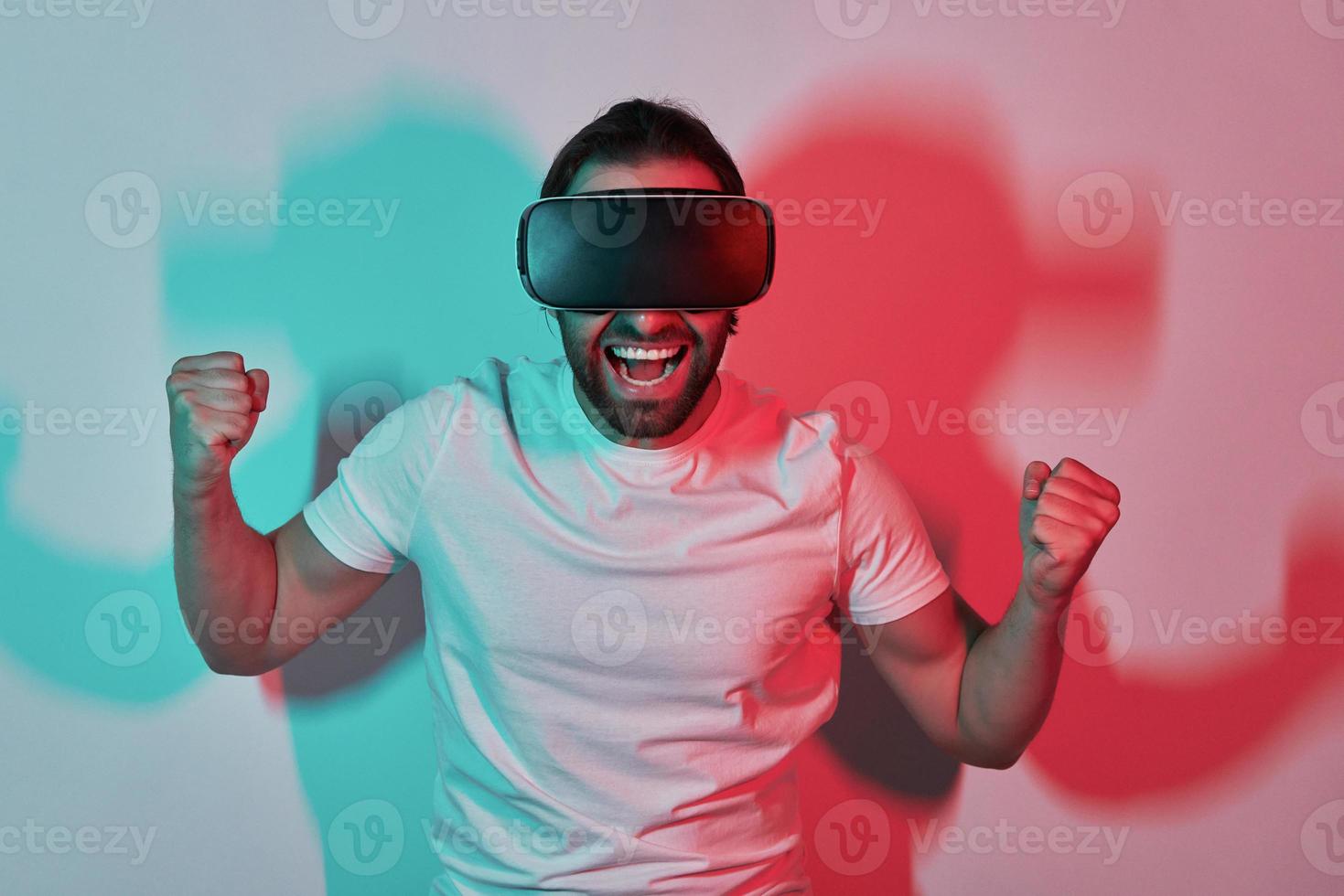 eccitato giovane uomo nel virtuale la realtà occhiali Esprimere a gesti con colorato ombre nel il sfondo foto