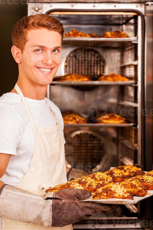 fresco al forno brioche per voi. bello giovane uomo nel grembiule assunzione il fresco al forno Cornetti a partire dal il forno e sorridente foto