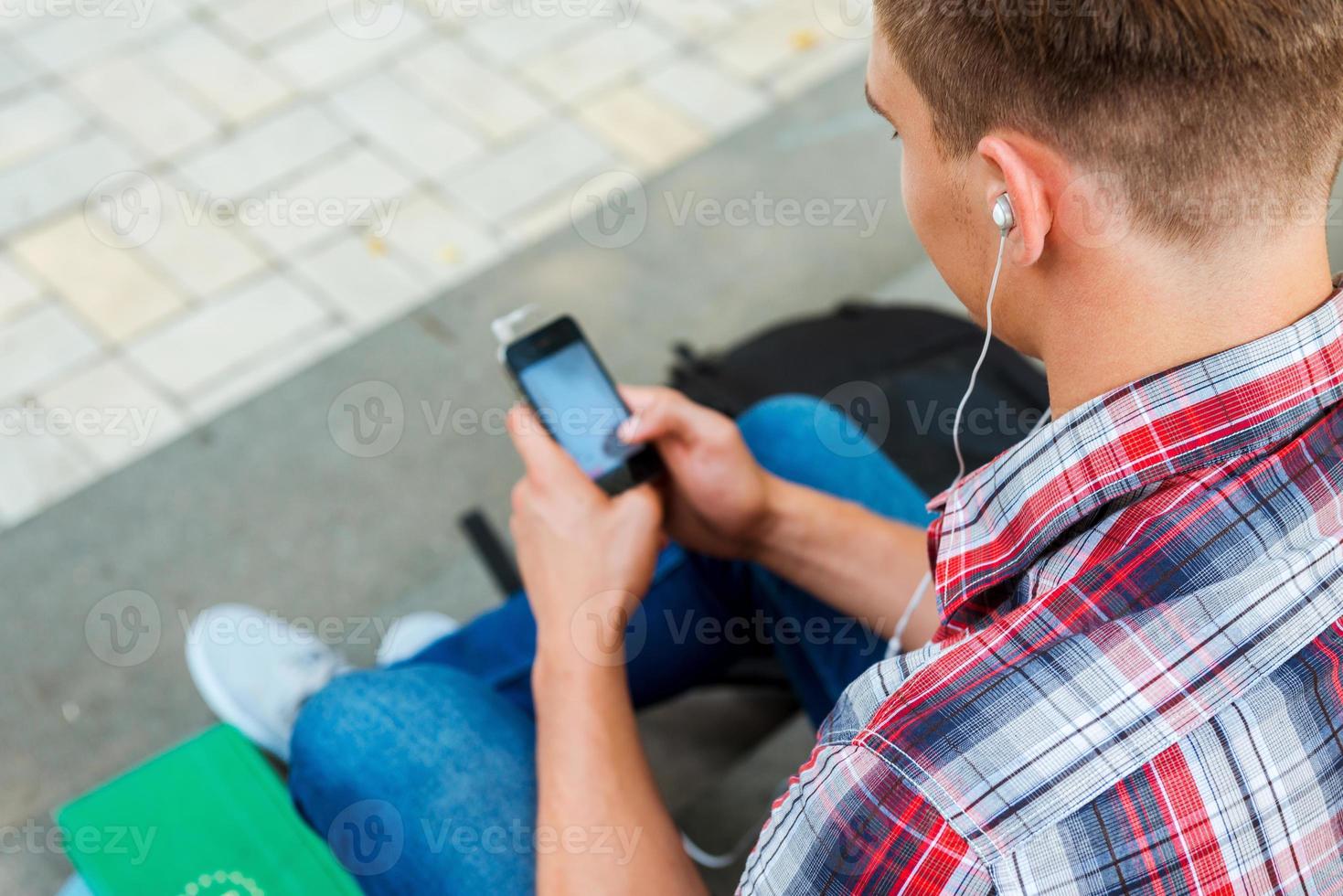 godendo musica all'aperto. superiore Visualizza di giovane uomo ascoltando per mp3 giocatore mentre seduta a il all'aperto scala foto