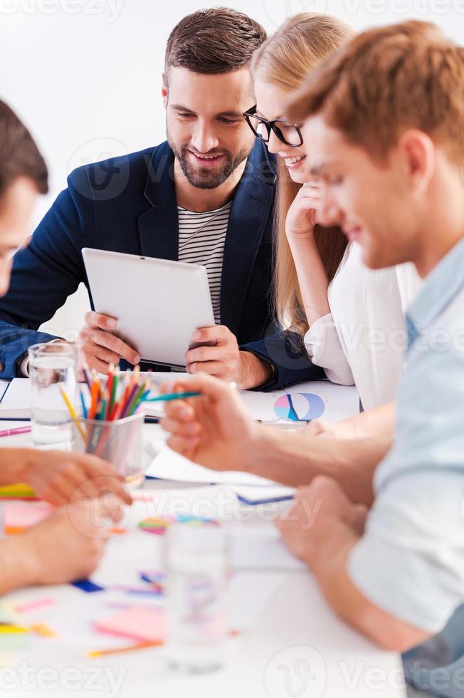 Lavorando momenti. gruppo di allegro attività commerciale persone nel inteligente casuale indossare Lavorando insieme mentre seduta a il tavolo foto