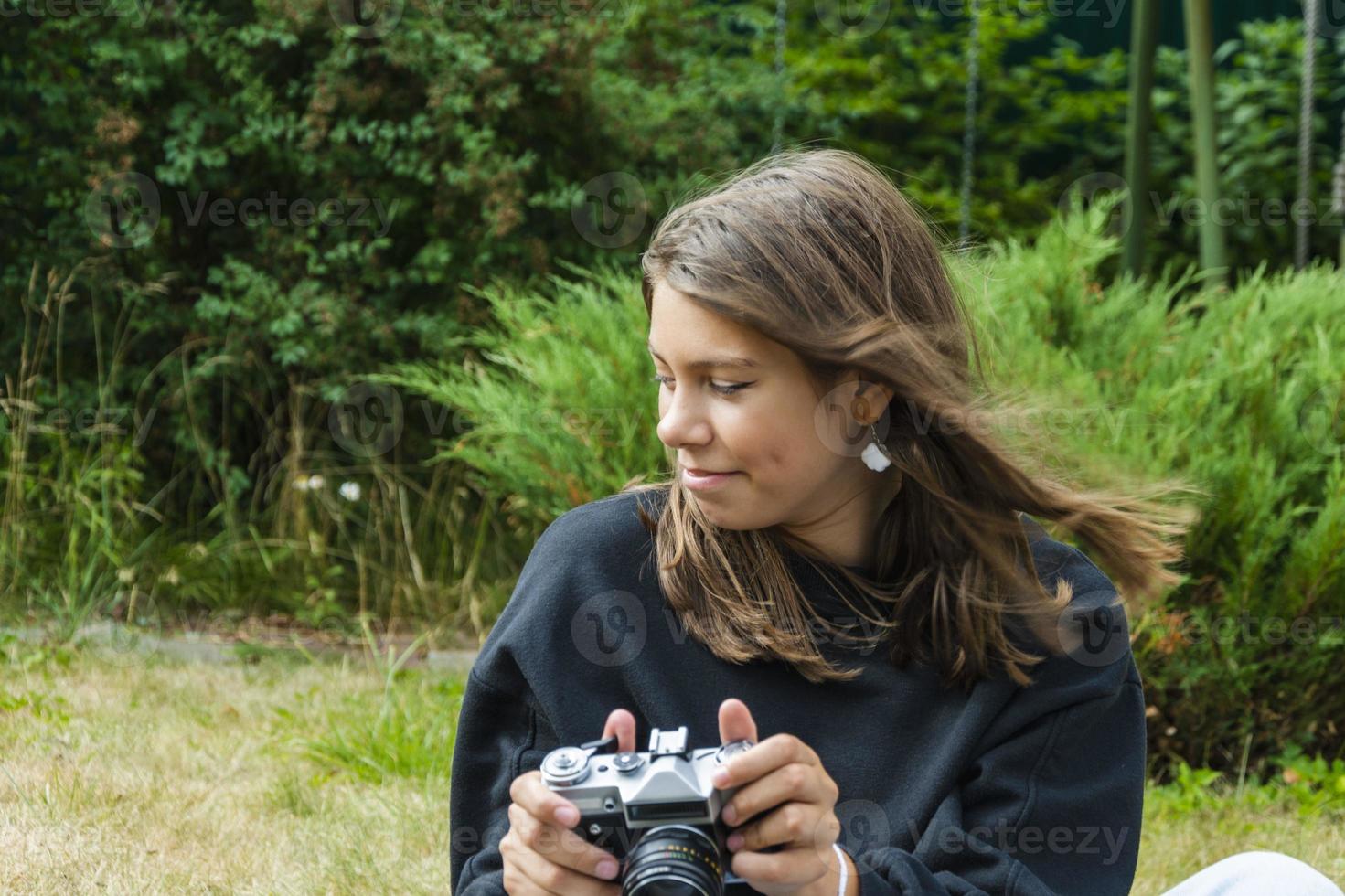 carino adolescente ragazza con un' telecamera, un' ragazza assunzione immagini su un' retrò Vintage ▾ telecamera su il erba nel il parco, un' passatempo concetto foto