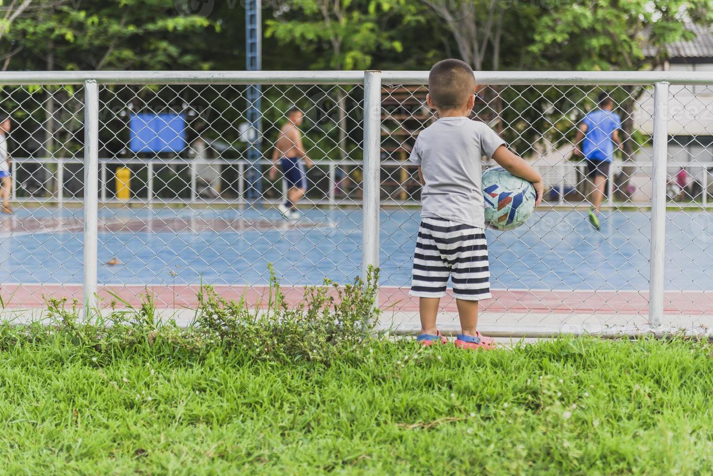 ragazzo Tenere un' calcio palla nel il suo mano a un' calcio campo poco bambini volere per giocare calcio. foto