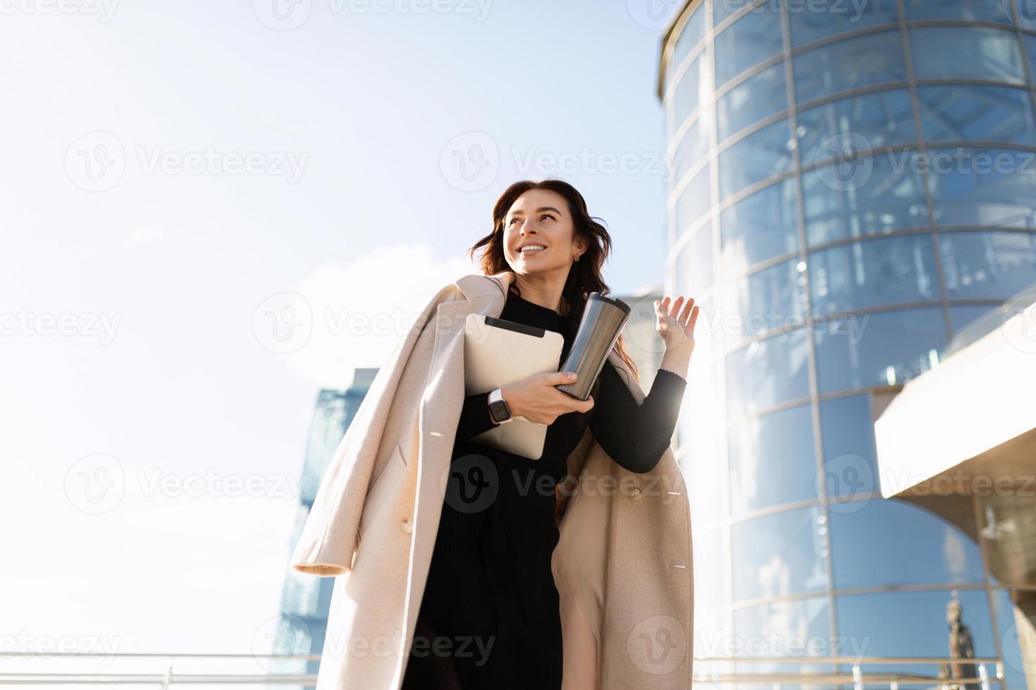 ritratto di un' riuscito giovane attività commerciale donna nel un' elegante cappotto contro il fondale di un ufficio grattacielo, donna capo nel attività commerciale concetto foto