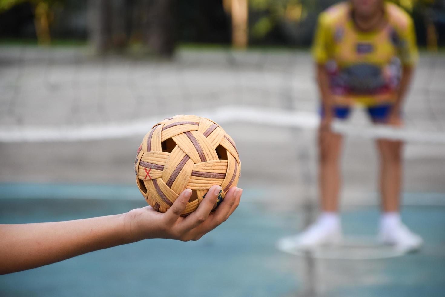 sepak takraw sfera, sud-est asiatico paesi tradizionale sport, Tenere nel mano di giovane asiatico femmina sepak takraw giocatore nel davanti di il netto prima lancio esso per un altro giocatore per calcio al di sopra di il rete. foto