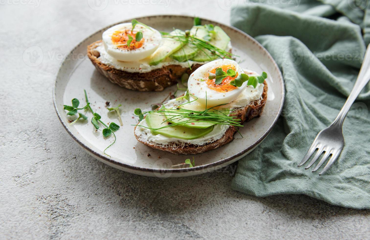 pane tostato, uova sode, fetta di avocado, microgreens su un piatto foto