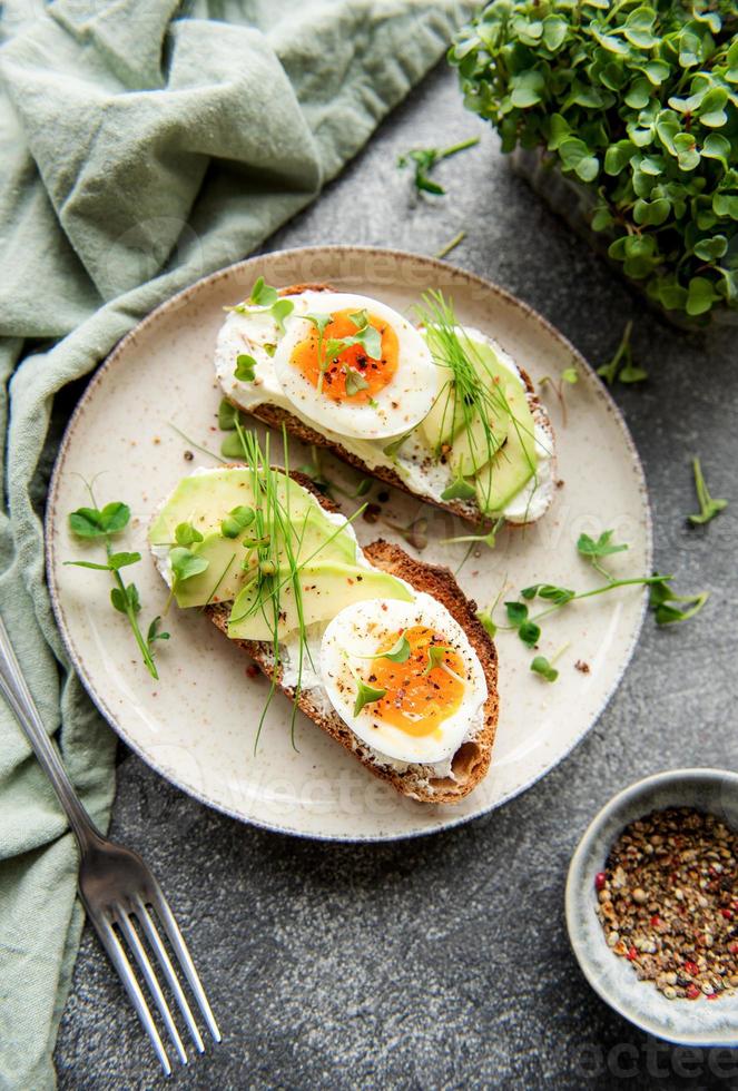 pane tostato, uova sode, fetta di avocado, microgreens su un piatto foto