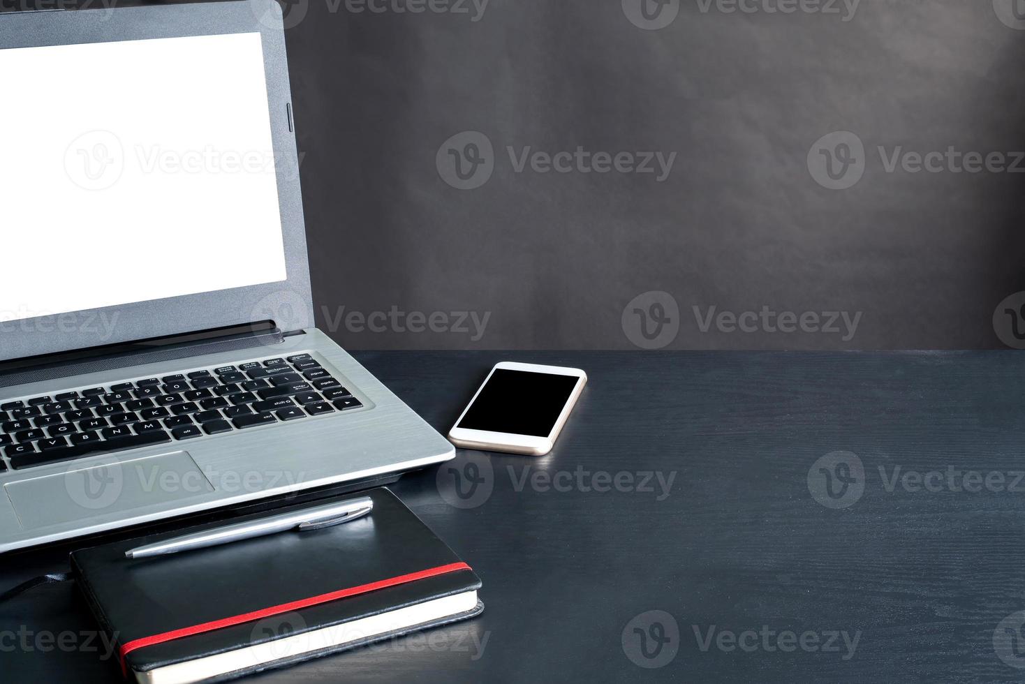 computer portatile, smartphone, taccuino, penna, su nero di legno tavolo con nero sfondo foto