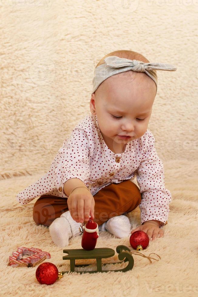 poco ragazza è giocando con Natale decorazioni su un' beige plaid. foto