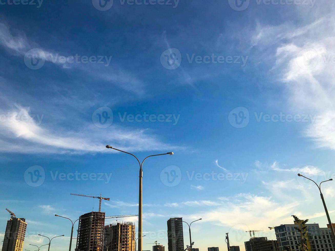 costruzione di un' nuovo la zona. gru siamo trasporto pesante calcestruzzo blocchi. nel il distanza, luci siamo visibile per illuminare il strada. case con panoramico vetri e individualizzato pittura foto