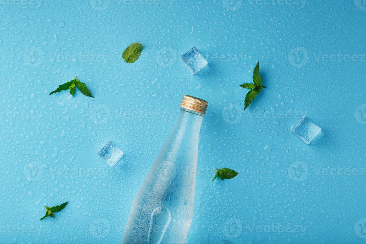 freddo acqua bottiglia, ghiaccio cubi, gocce e menta le foglie su un' blu sfondo. foto