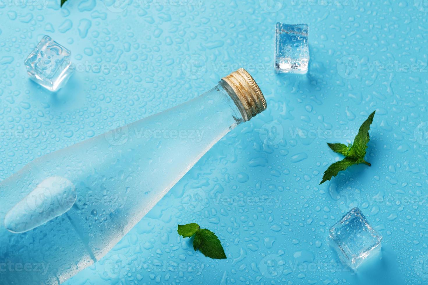 bottiglia con un ghiaccio freddo bevanda, ghiaccio cubi, gocce e menta le foglie su un' blu sfondo. foto