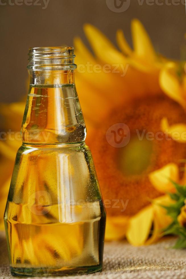 girasole olio nel un' bicchiere bottiglia e fiori su un' di legno sfondo, avvicinamento. foto