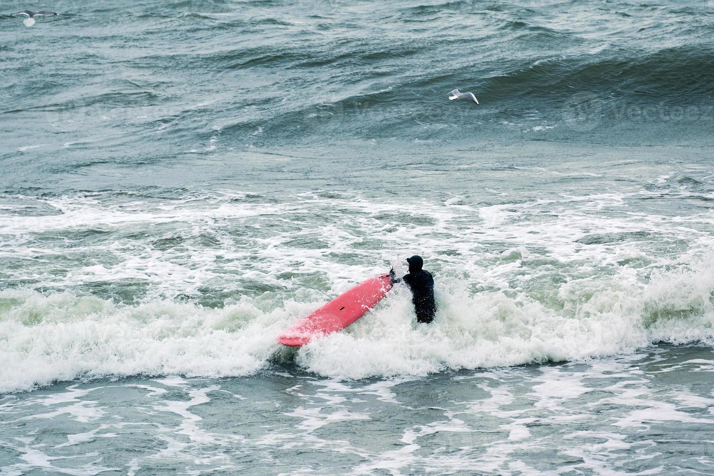 surfista maschio in costume da bagno nelle onde del mare con tavola da surf rossa foto