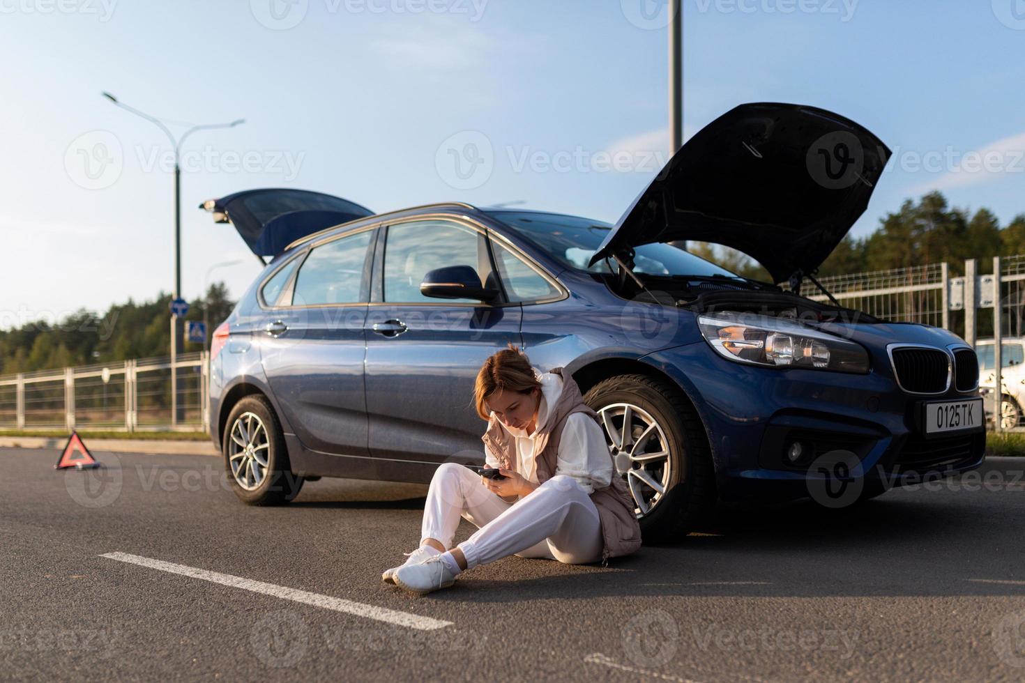 giovane donna in attesa per Aiuto seduta vicino un' rotto giù auto su il strada foto