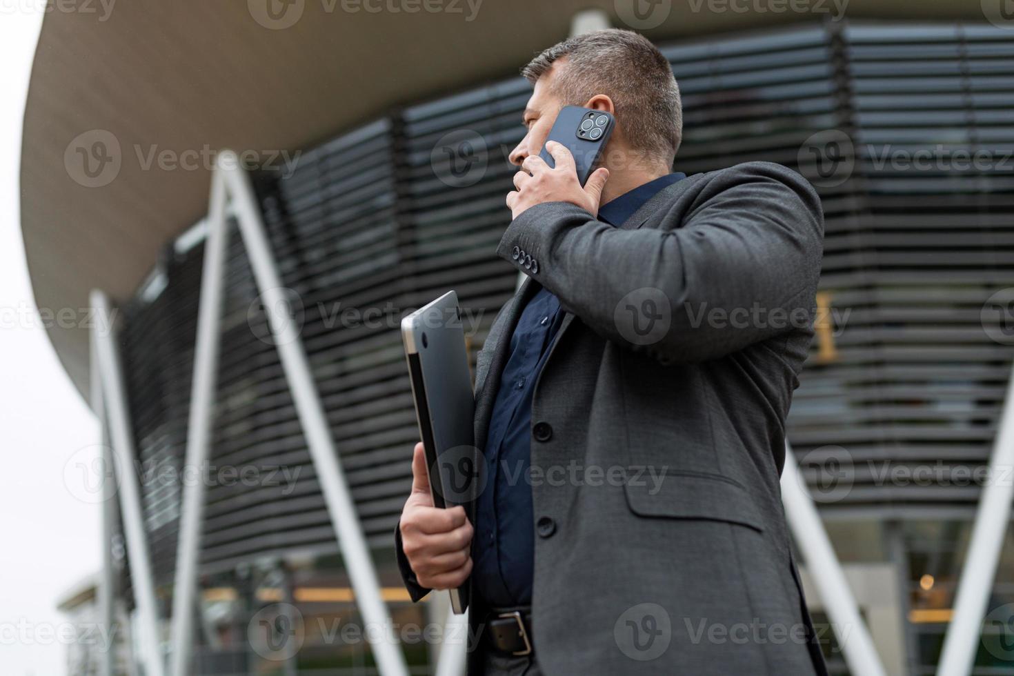 maschio uomo d'affari parlando su un' mobile Telefono contro il fondale di un ufficio costruzione, concetto di un' riuscito vero tenuta agente foto