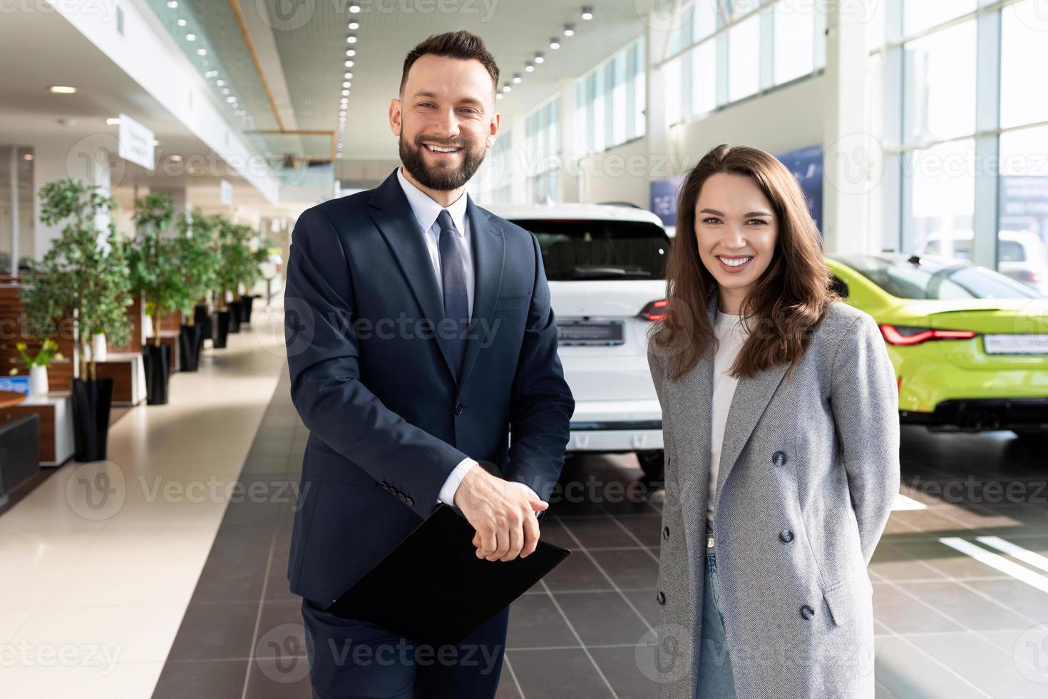 soddisfatto acquirente e venditore di un' auto concessionaria centro su il sfondo di nuovo macchine, il concetto di acquisto un' auto su contratto di locazione foto