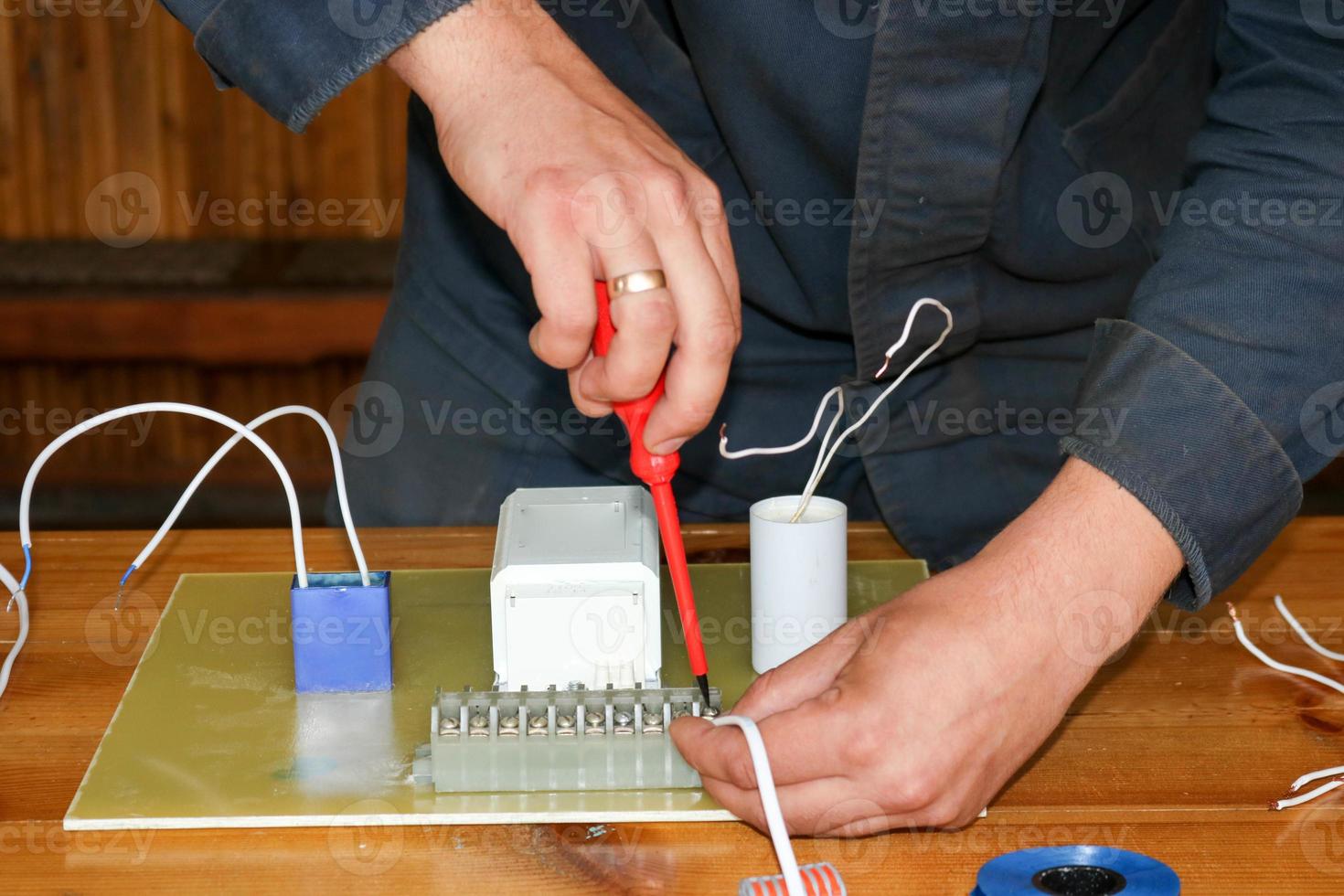 un' uomo Lavorando elettricista lavori, raccoglie il elettrico circuito di un' grande bianca strada lampada con fili, un' relè a un industriale pianta fabbrica foto
