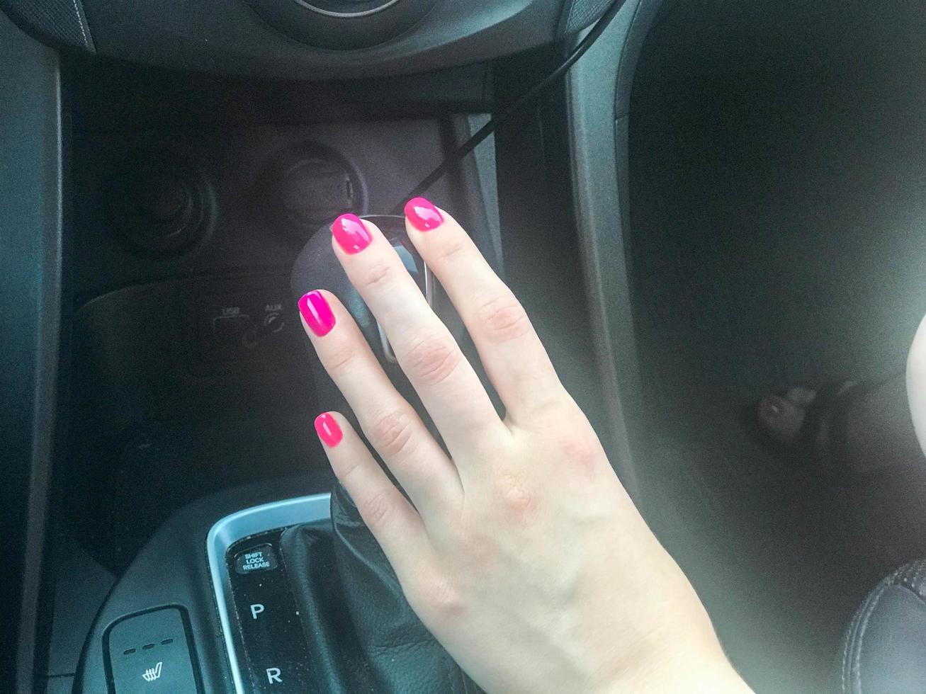 donna ragazza con un' bellissimo manicure rosa Chiodi è Tenere un' Ingranaggio leva nel un' riduttore auto dietro a il ruota. amore strada viaggio foto