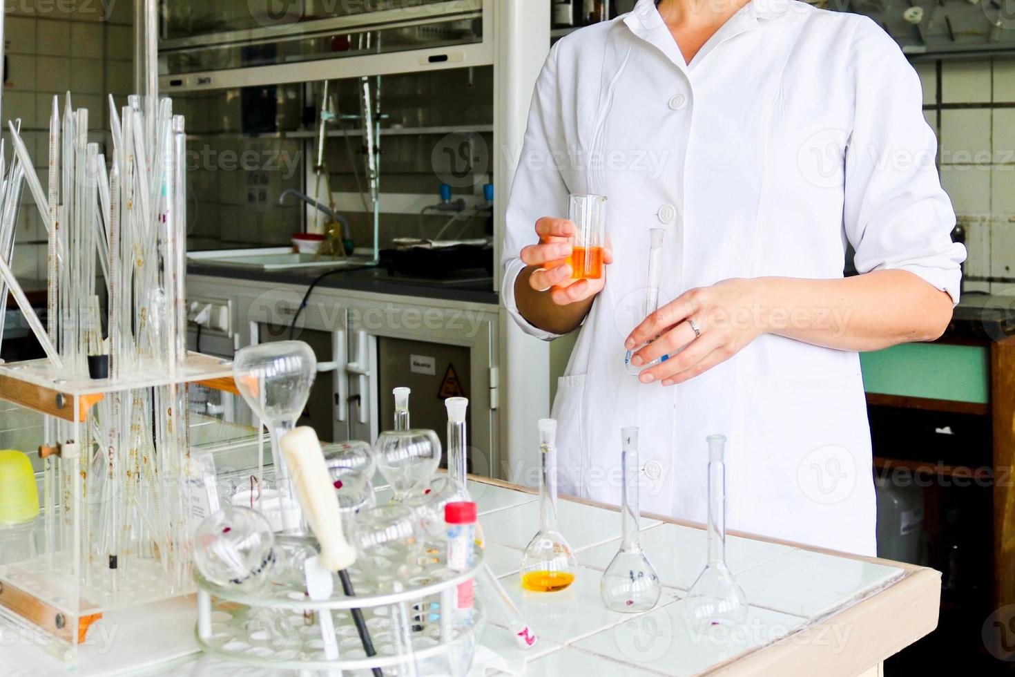 un' femmina laboratorio assistente, un' medico, un' chimico, lavori con boccette, test tubi, fa soluzioni, medicinali, miscele il ingredienti nel il laboratorio. laboratorio assistente trasporta su il ricerca foto