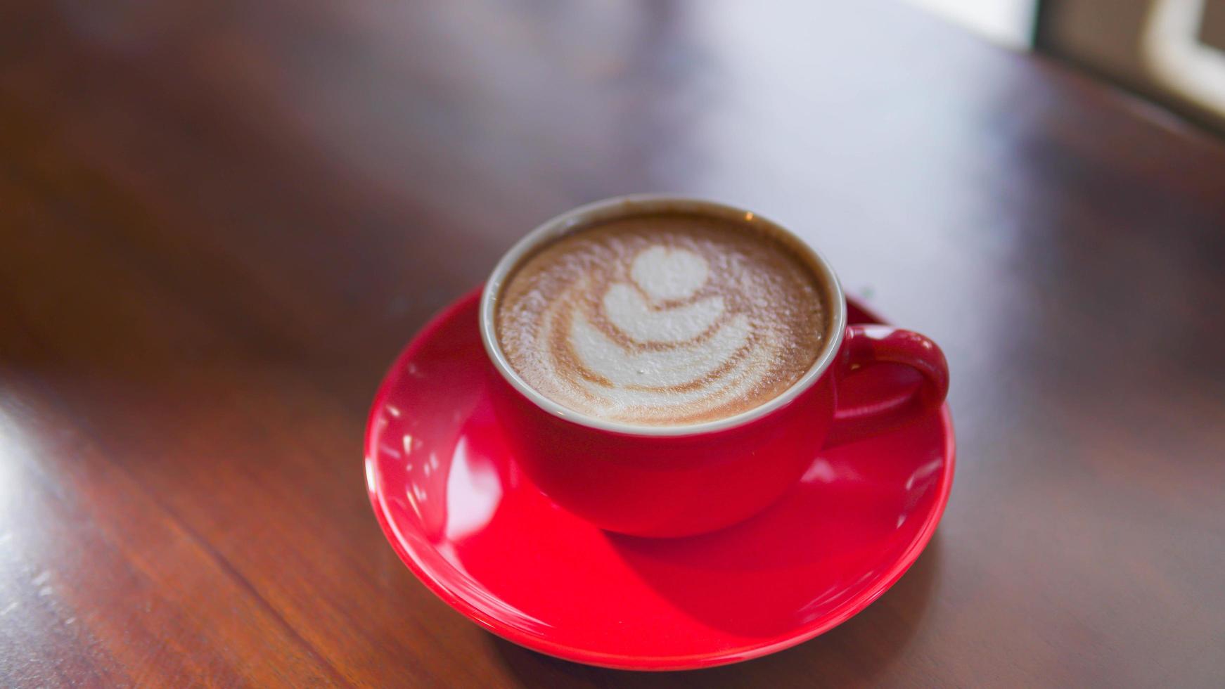 vicino su rosso caffè tazza con cuore forma latte macchiato arte su legna tavolo foto