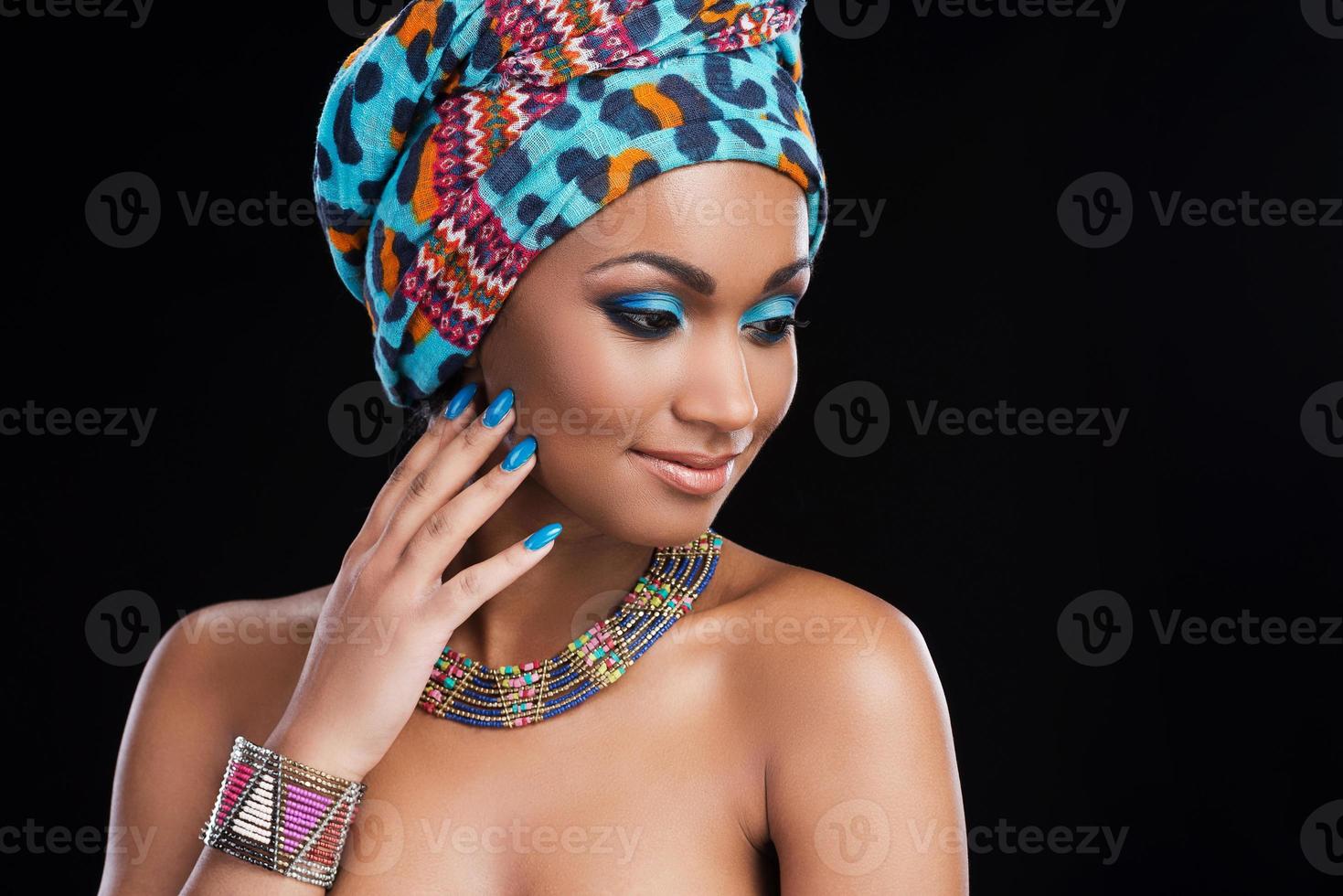 africano bellezza. bellissimo africano donna indossare un' foulard e collana e guardare lontano mentre in piedi contro nero sfondo foto