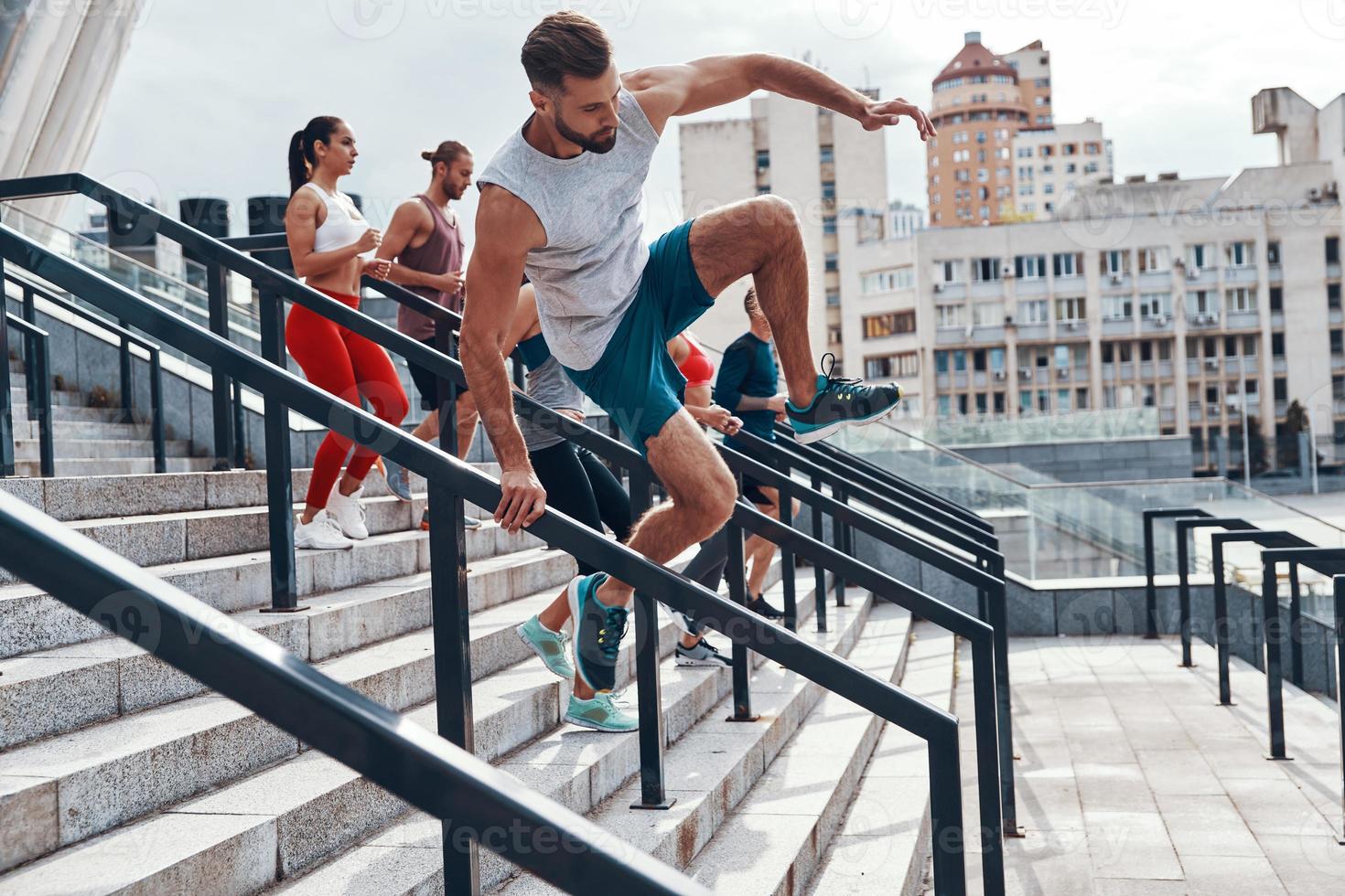 giovane uomo nel gli sport capi di abbigliamento salto mentre esercizio con il suo amici su il le scale all'aperto foto