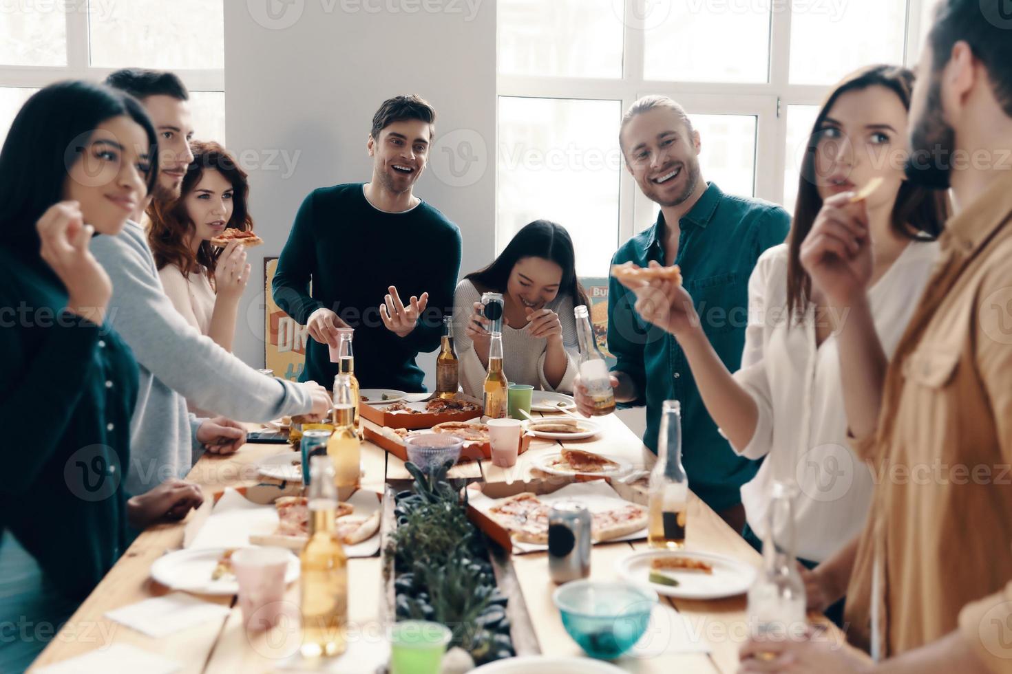 Pizza festa. gruppo di giovane persone nel casuale indossare mangiare Pizza e sorridente mentre avendo un' cena festa in casa foto