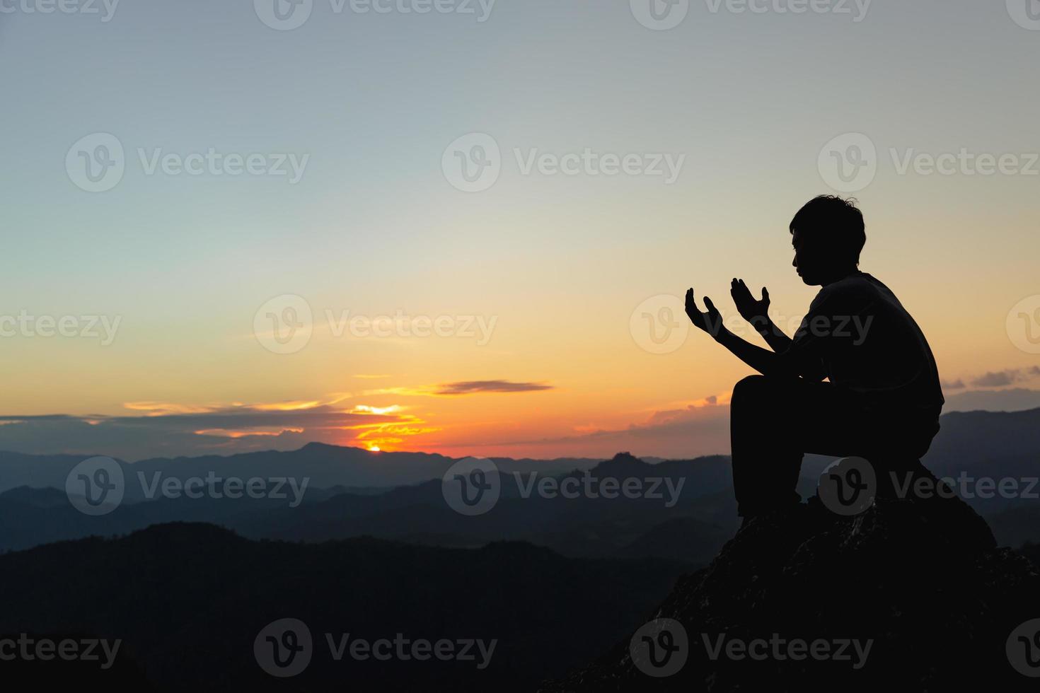 silhouette di un' giovane uomo preghiere per Dio su il montagna a tramonto sfondo. donna raccolta il suo mani nel culto. cristiano religione concetto. foto