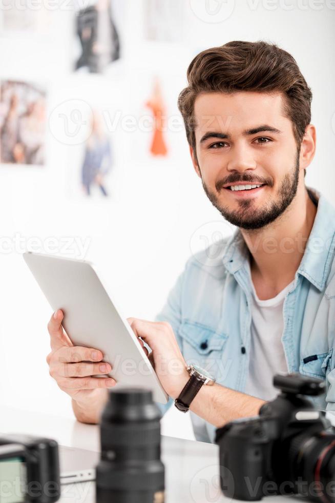 Lavorando su creativo progetto. sorridente giovane uomo Lavorando su digitale tavoletta mentre seduta a il suo Lavorando posto foto