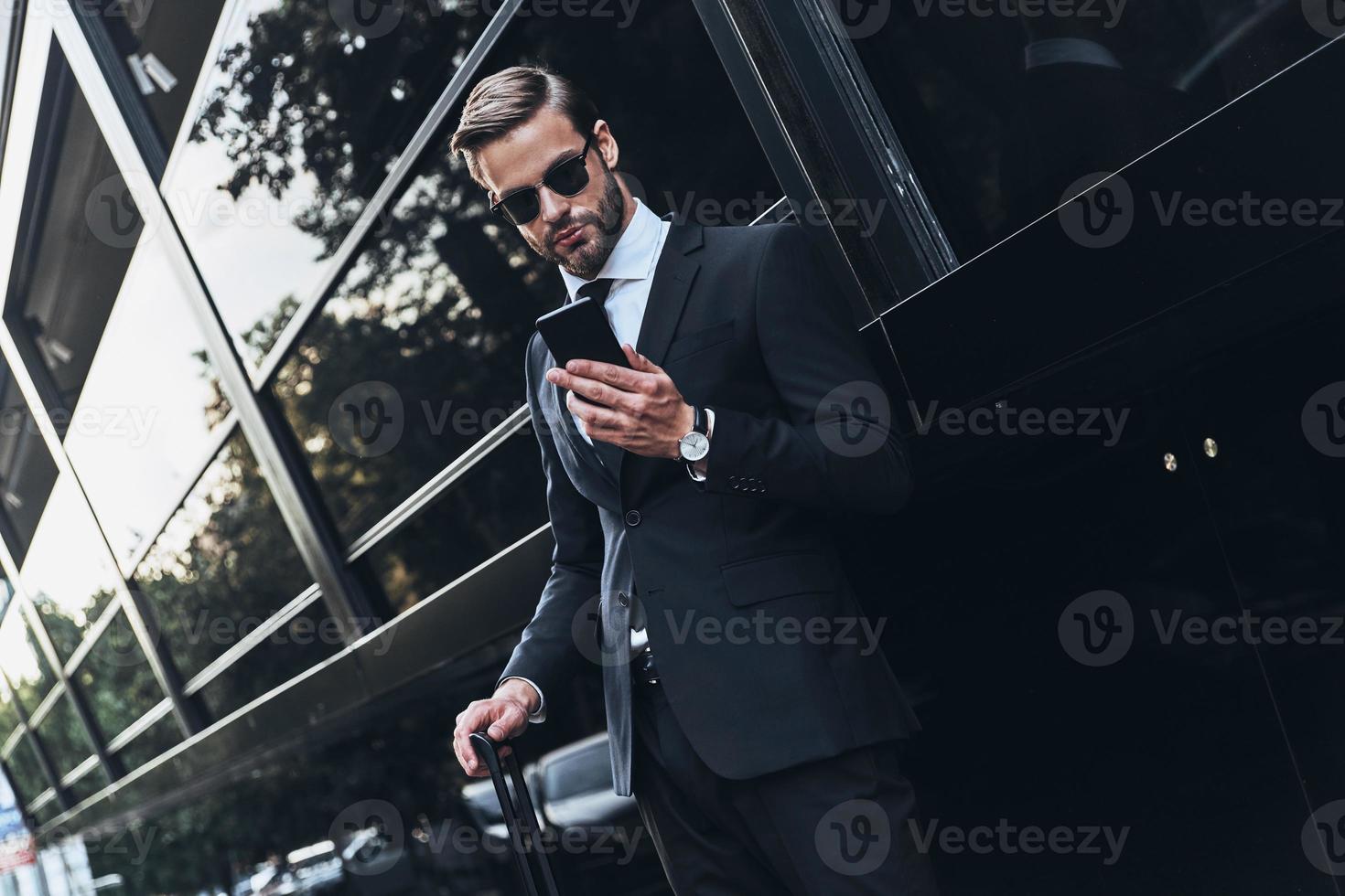 Chiacchierare con cliente. bene guardare giovane uomo nel pieno completo da uomo utilizzando il suo inteligente Telefono mentre in piedi all'aperto foto