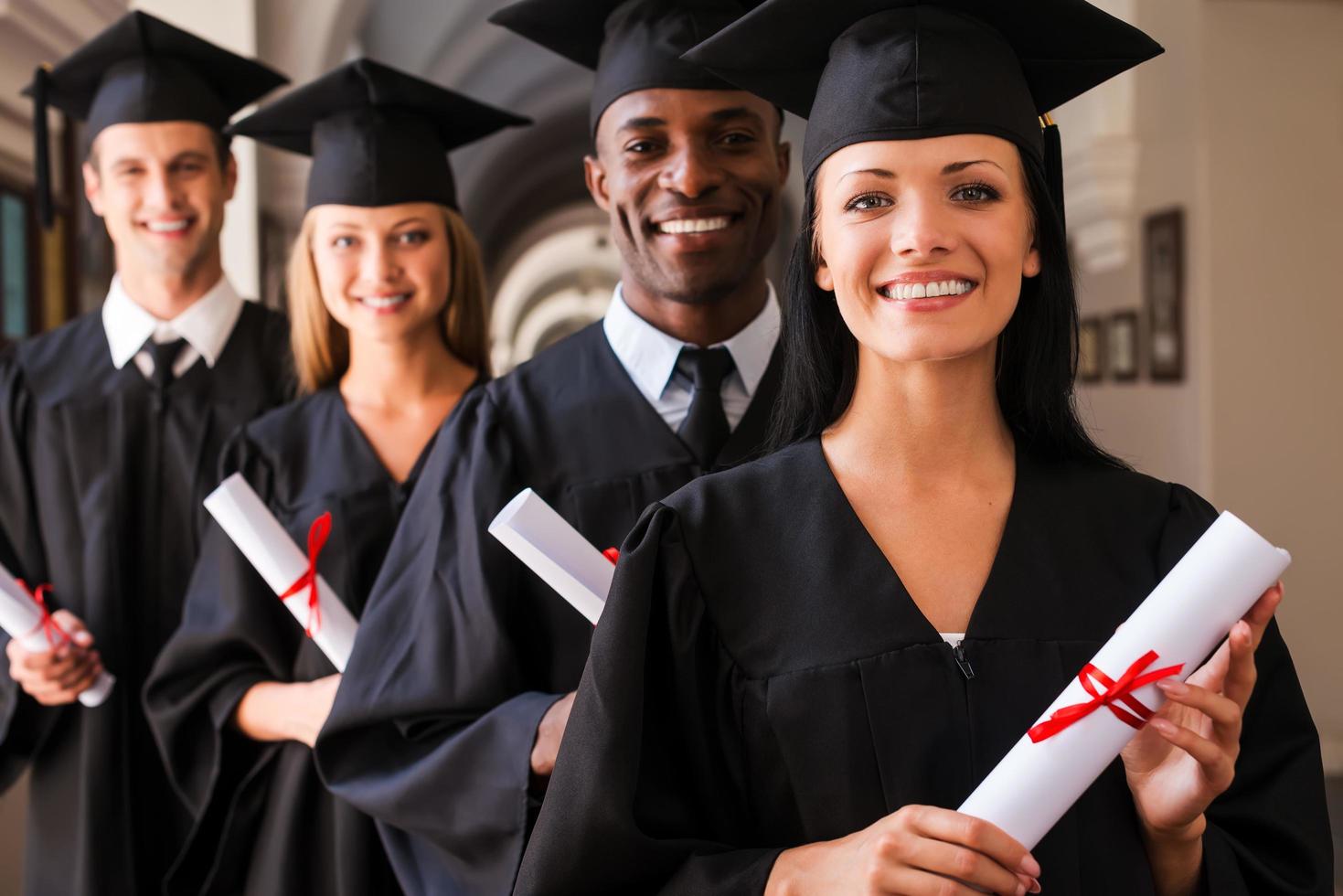 pronto per successo. quattro Università laureati in piedi nel un' riga e sorridente foto