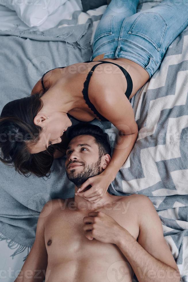 semplicemente nel amore. superiore Visualizza di bellissimo giovane semivestito coppia dire bugie viso per viso mentre la spesa tempo nel il Camera da letto foto