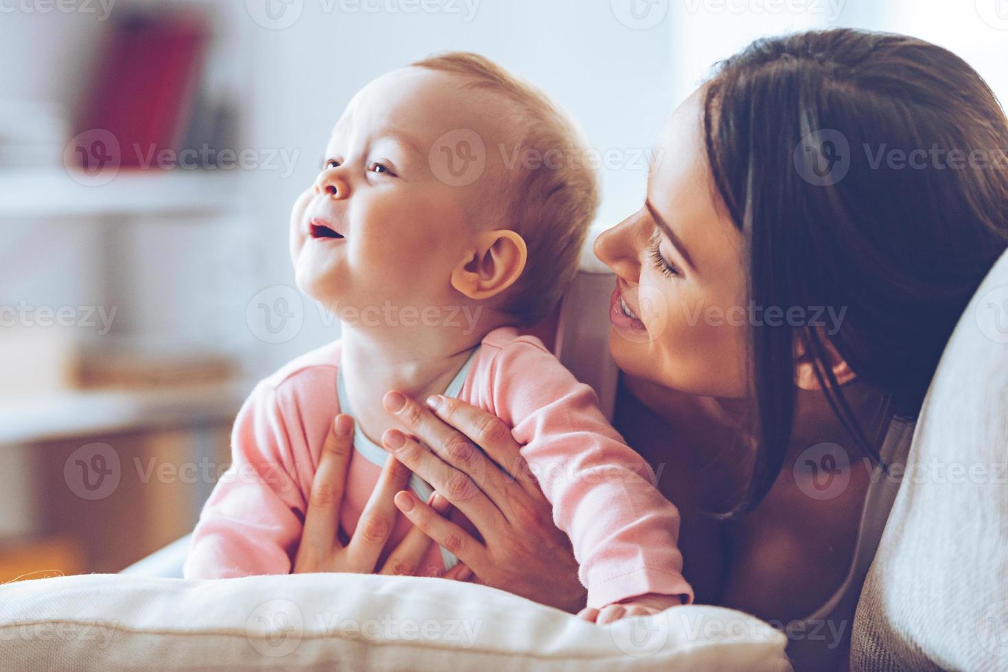 esso è così simpatico per trascorrere tempo con mammina. allegro giovane donna abbracciare sua bambino ragazza e guardare a sua con amore mentre seduta su il divano a casa foto