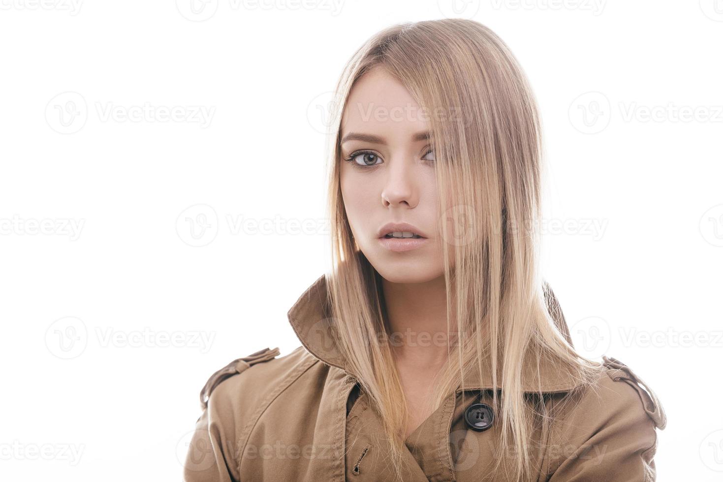 elegante bellezza. ritratto di attraente giovane donna nel cappotto guardare a telecamera mentre in piedi contro bianca sfondo foto