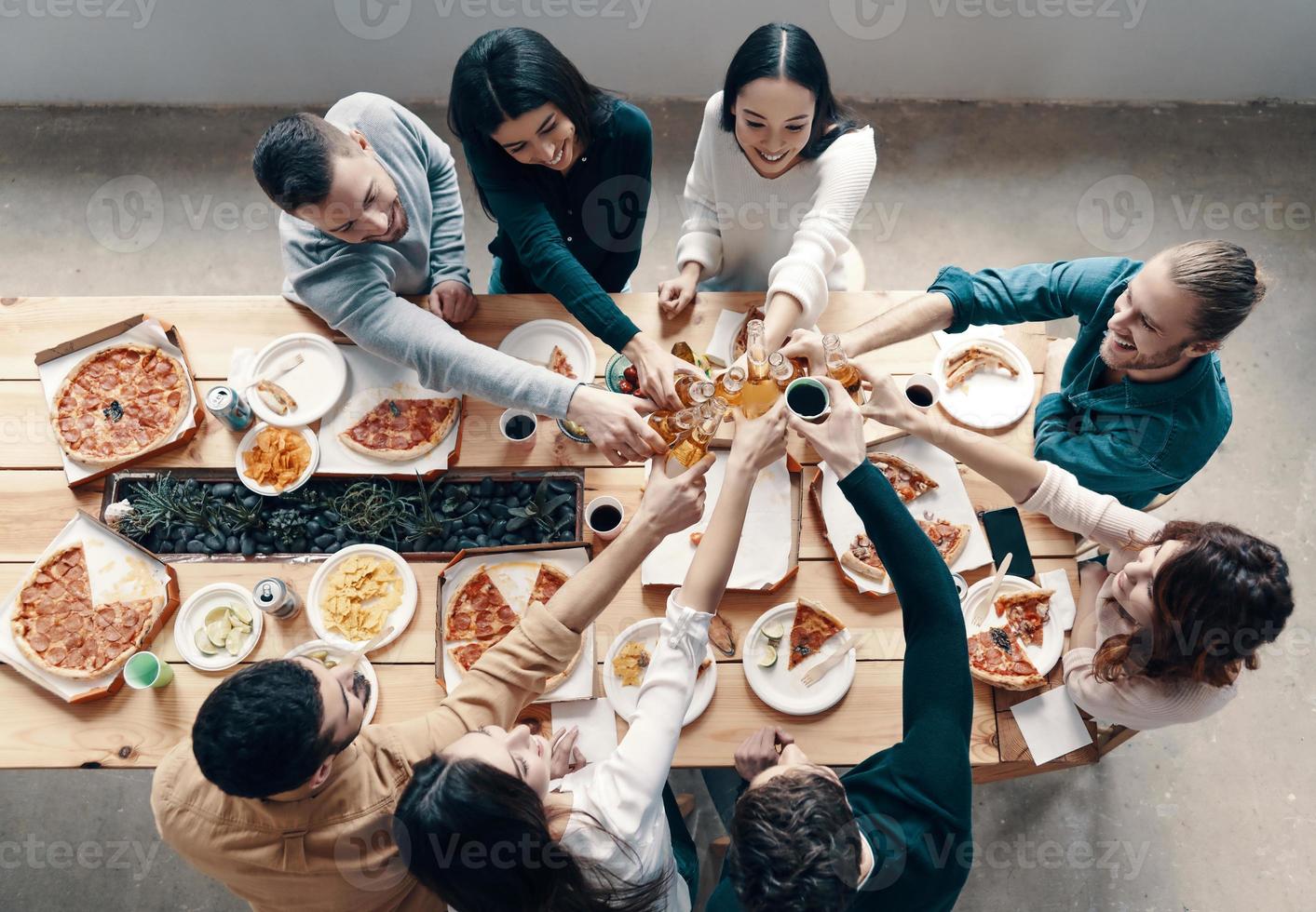 gruppo di giovane persone nel casuale indossare raccolta Pizza e sorridente mentre avendo un' cena festa in casa foto