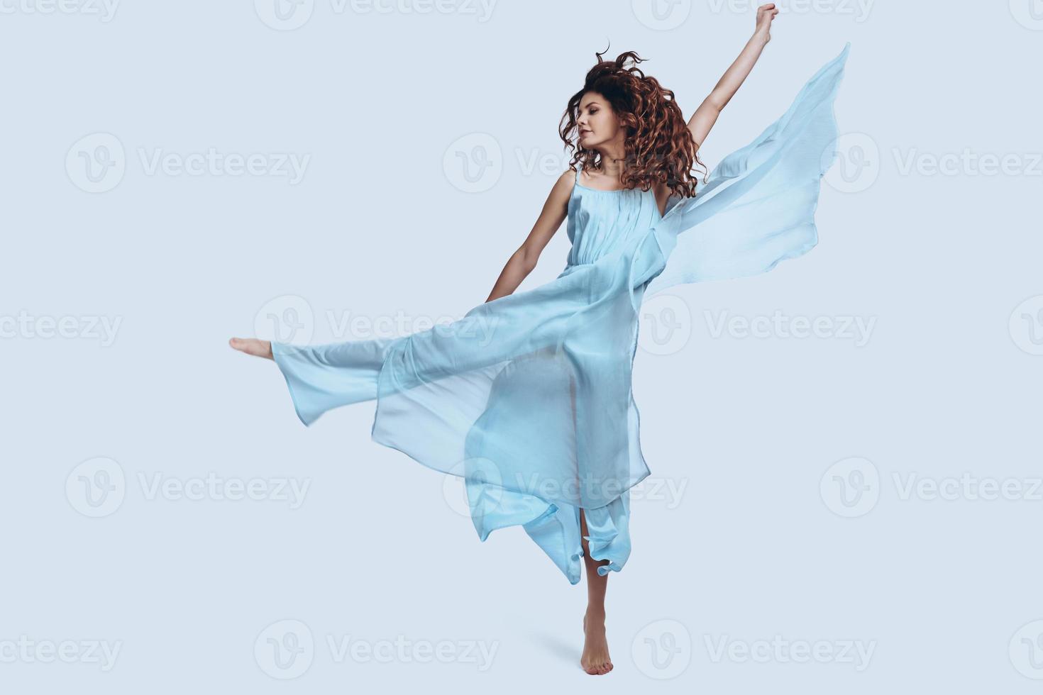 estremamente Bellissima. pieno lunghezza studio tiro di attraente giovane donna nel elegante vestito Esprimere a gesti e sorridente mentre salto contro grigio sfondo foto