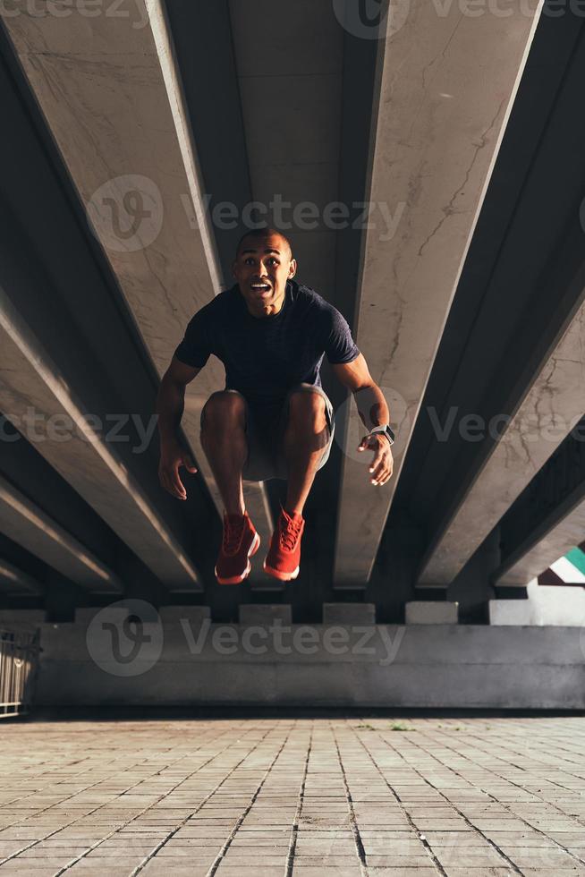 migliore esercizio. bello giovane africano uomo nel gli sport capi di abbigliamento salto e sorridente mentre esercizio all'aperto foto