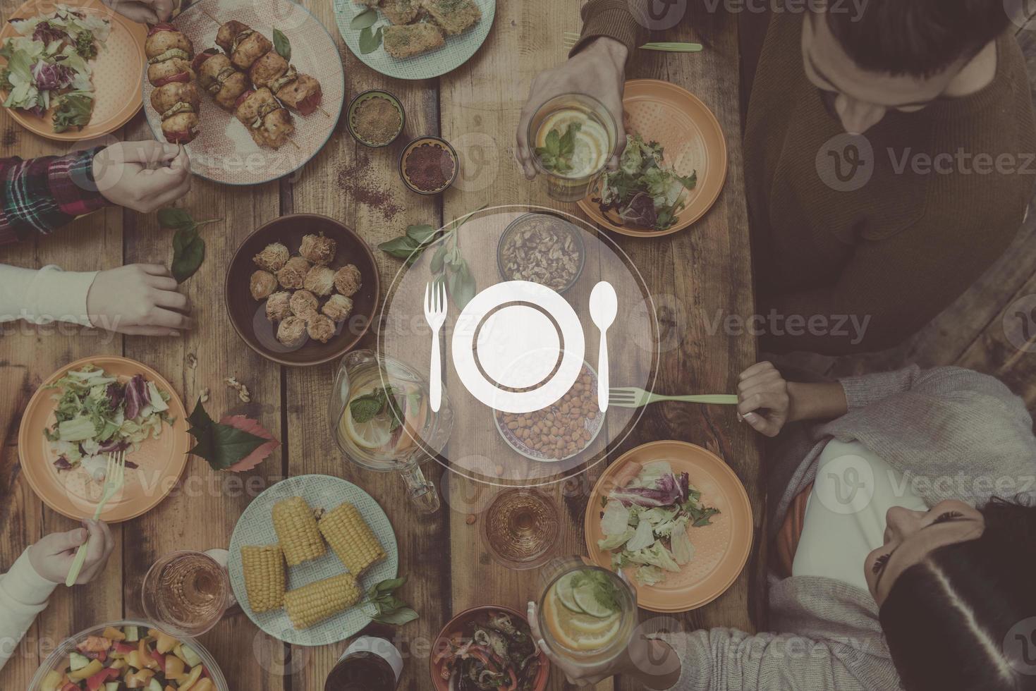 ottenere insieme per cena. digitalmente composto immagine di cucina utensile al di sopra di superiore Visualizza di quattro persone avendo cena insieme mentre seduta a il rustico di legno tavolo foto