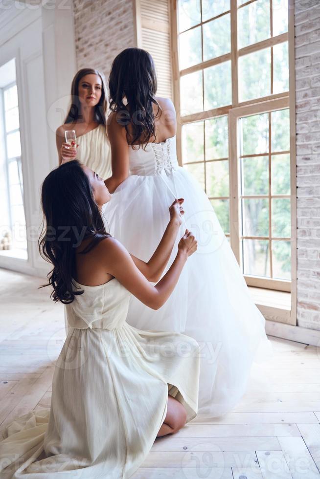 battere amici siamo sempre intorno a. pieno lunghezza di damigella d'onore legatura un' corsetto di un' nozze vestito mentre porzione un' bellissimo sposa nel il adattamento camera foto