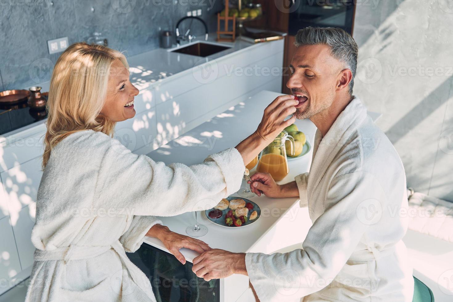 superiore Visualizza di bellissimo maturo coppia nel accappatoi godendo prima colazione insieme mentre la spesa tempo nel il domestico cucina foto