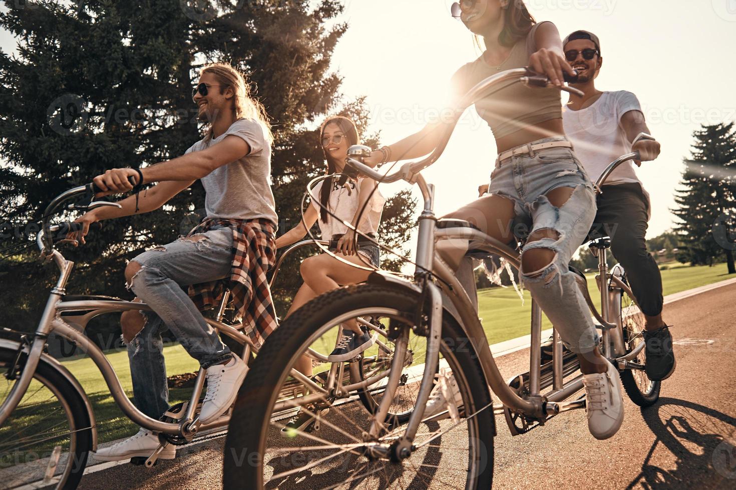 caldo sole e un' grande azienda. gruppo di contento giovane persone nel casuale indossare sorridente mentre Ciclismo insieme all'aperto foto