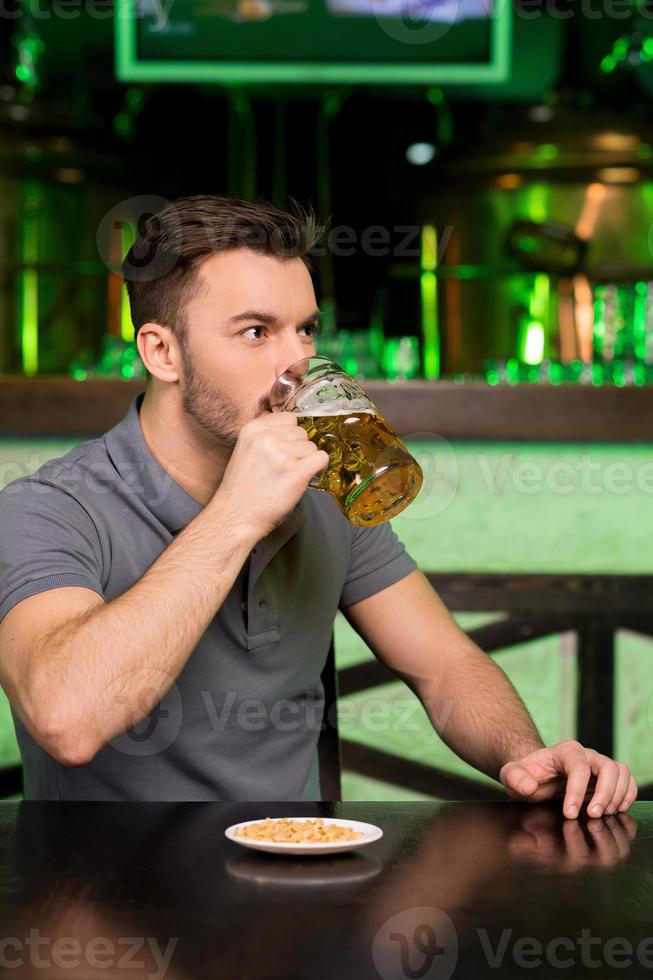 potabile fresco birra. riflessivo giovane uomo potabile birra e guardare lontano mentre seduta nel bar foto