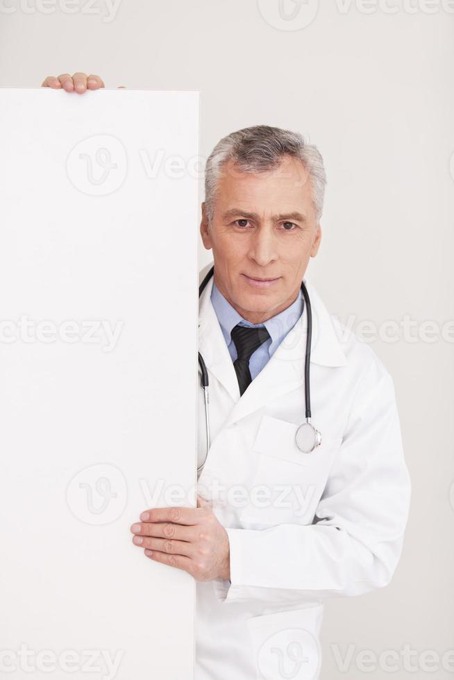 medico con copia spazio. anziano grigio capelli medico nel uniforme guardare su di copia spazio e sorridente mentre isolato su bianca foto