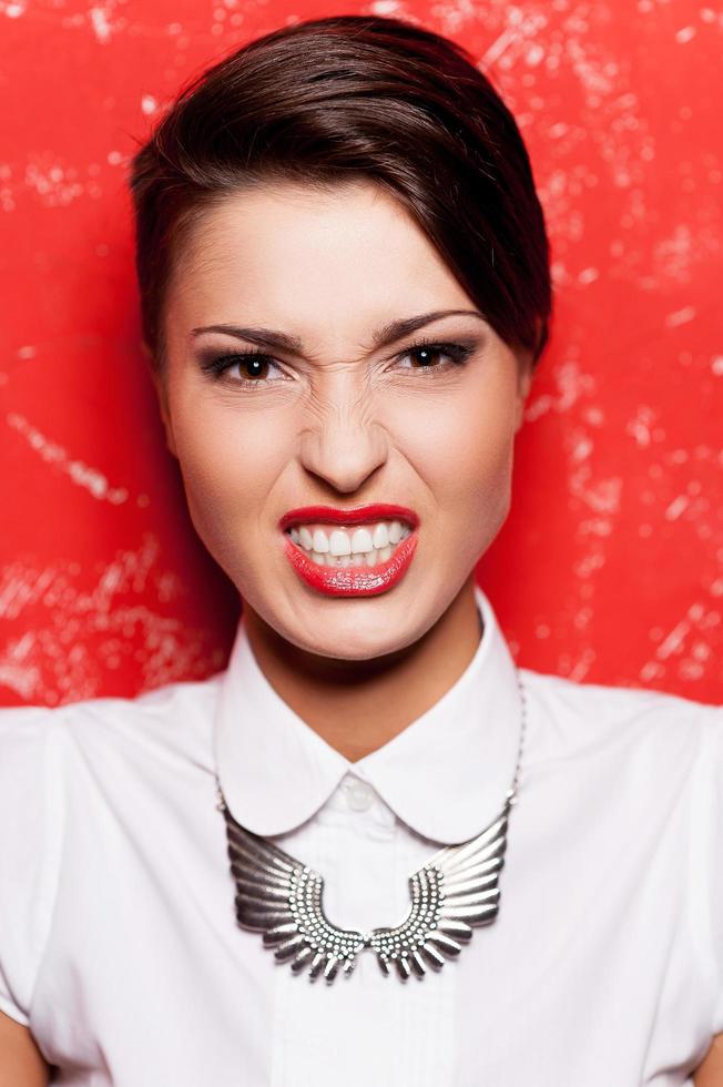 veramente cattivo ragazza. bellissimo giovane corto capelli donna nel bianca camicia in posa contro rosso sfondo foto