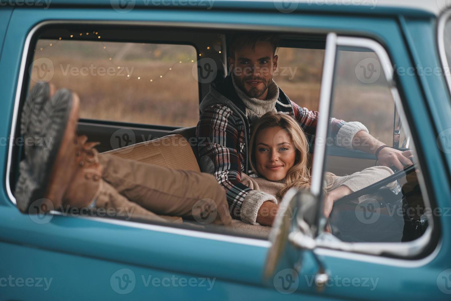 migliore viaggio mai. attraente giovane donna riposo e sorridente mentre sua fidanzato guida retrò stile mini furgone foto