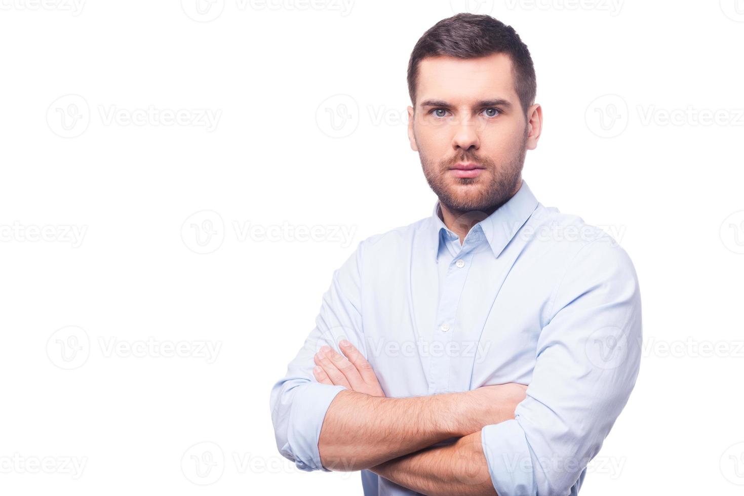 pronto per fare grande le cose. bello giovane uomo nel camicia guardare a telecamera e conservazione braccia attraversato mentre in piedi contro bianca sfondo foto