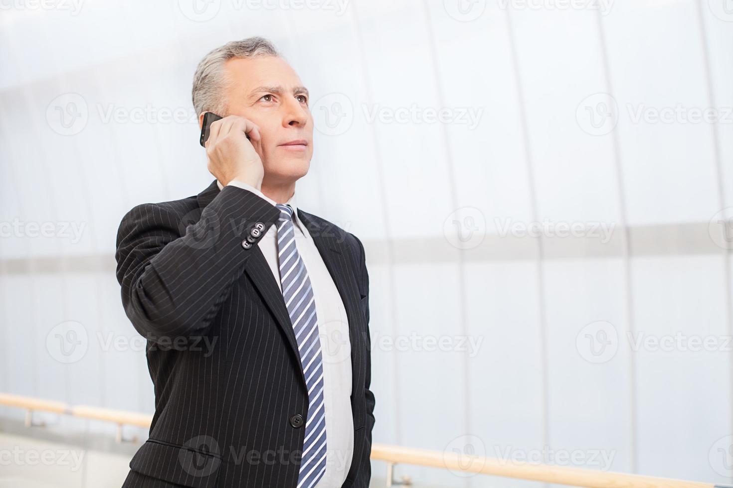 fiducioso esecutivo. fiducioso anziano uomo nel vestito formale parlando su il mobile Telefono e guardare lontano foto