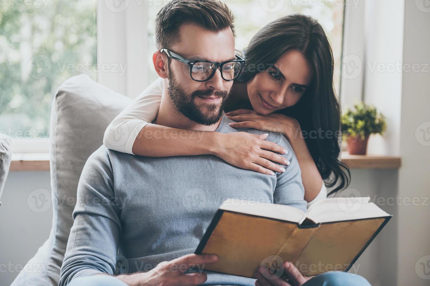 lettura loro preferito libro. bellissimo giovane donna bonding per sua marito mentre lui è lettura un' libro su il divano foto